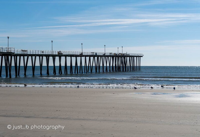 Fishing pier at low tide extending out into calm Atlantic ocean on a cold winter day.