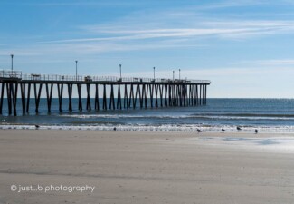Fishing pier at low tide extending out into calm Atlantic ocean on a cold winter day.