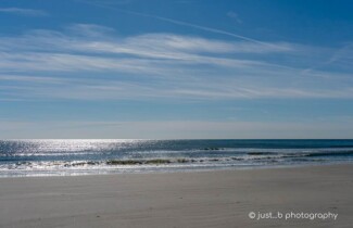 Winter beach scene with sun reflections on calm Atlantic ocean.
